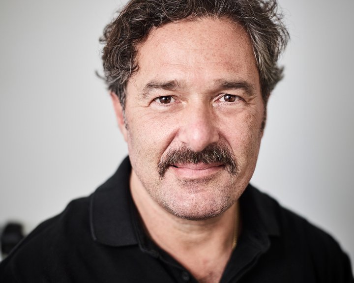 Porträt von Dr. med. Ioannis Theofylaktopoulos, ein freundlich blickender Mann mit dunklem, lockigem Haar und Schnurrbart in einem schwarzen Poloshirt.