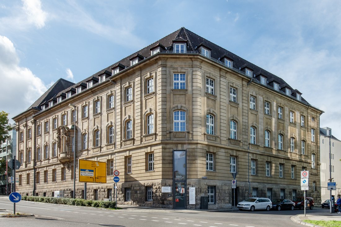Außenansicht eines markanten, mehrstöckigen Eckgebäudes aus hellem Sandstein mit klassischer Architektur, in dem sich eine moderne Augenpraxis befindet.