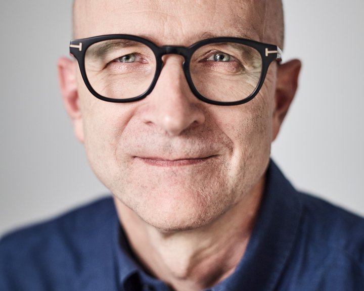 Porträt von Dr. med. Burkhard Schloßmacher, ein lächelnder Mann mit Glatze und markanter schwarzer Brille vor hellem Hintergrund.