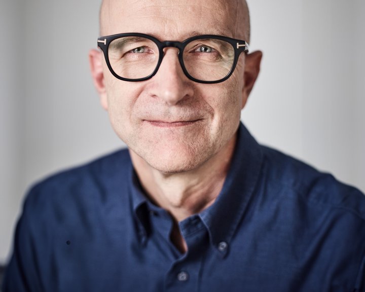 Porträt von Dr. med. Burkhard Schloßmacher, ein lächelnder Mann mit Glatze und markanter schwarzer Brille vor hellem Hintergrund.