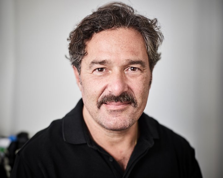 Porträt von Dr. med. Ioannis Theofylaktopoulos, ein freundlich blickender Mann mit dunklem, lockigem Haar und Schnurrbart in einem schwarzen Poloshirt.