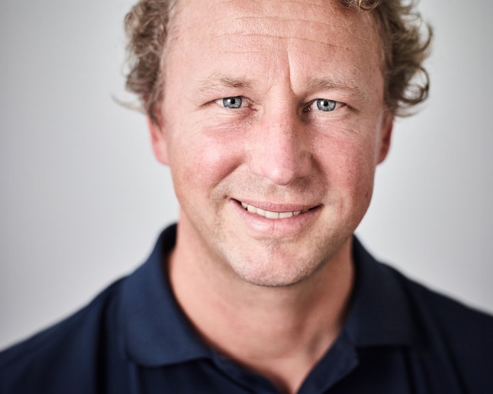 Porträt von Dr. med. Per André Steinfeld, einem lächelnden Mann mit blondem, lockigem Haar und blauen Augen vor einem neutralen, hellen Hintergrund.