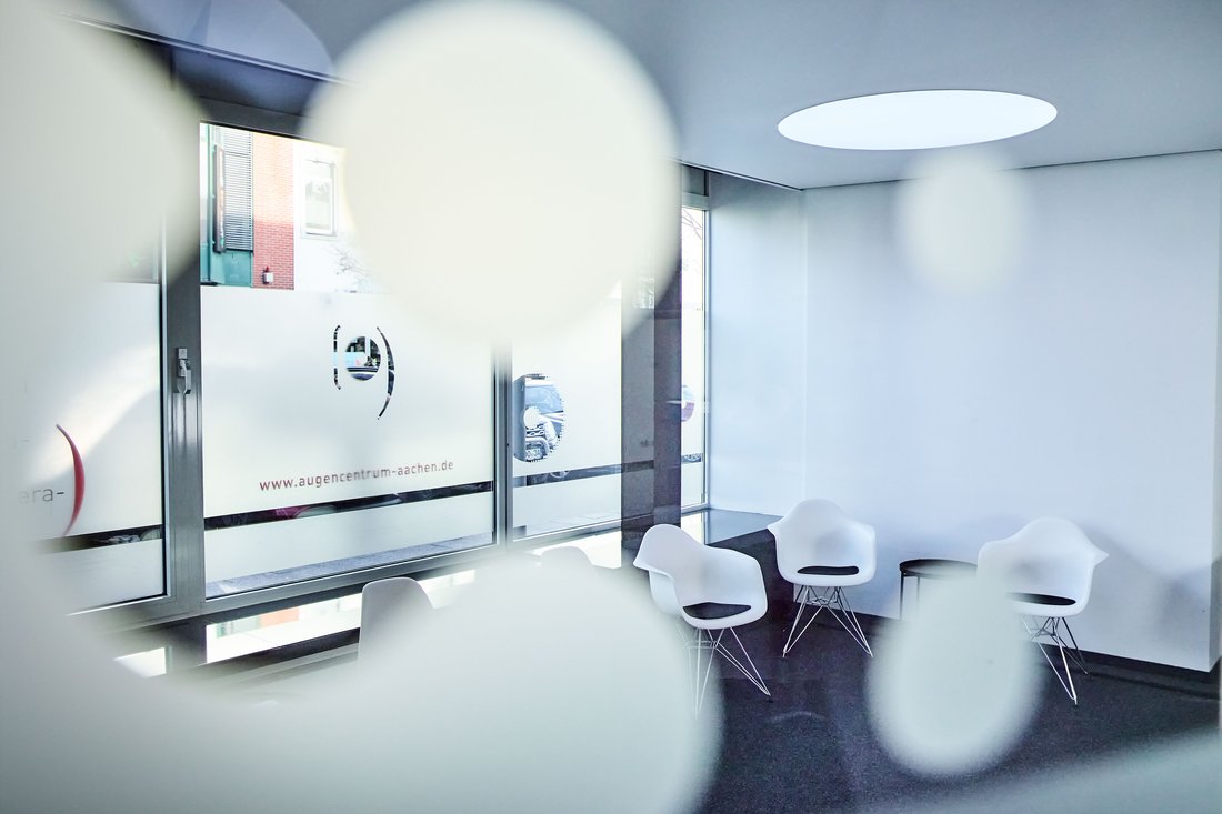 Ein heller, moderner Wartebereich in einer Praxis mit weißen Design-Sesseln vor einer Fensterfront, die mit dezenten Sichtschutz-Folien und dem Praxis-Logo gestaltet ist.