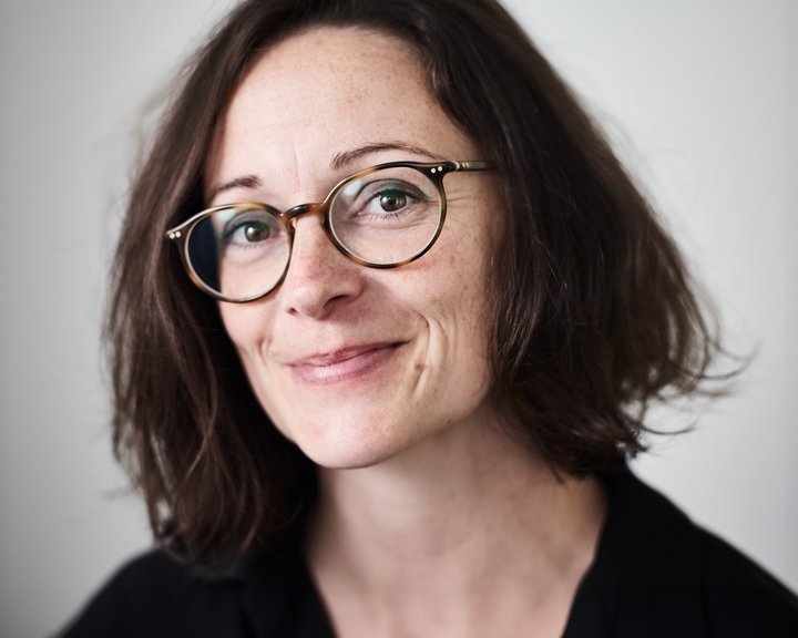 Porträt von Dr. med. Estelle Ihry-Wolff, einer lächelnden Augenärztin mit braunem Haar und Brille vor hellem Hintergrund.